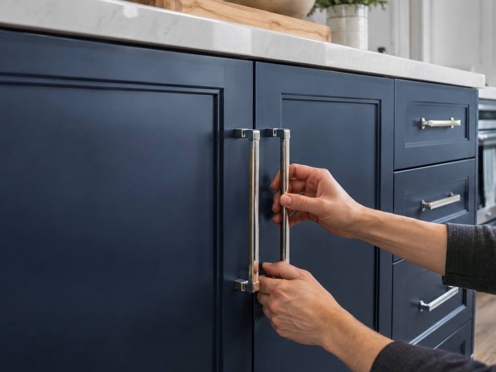 Hands fitting chrome bar handles onto navy blue painted cabinet doors
